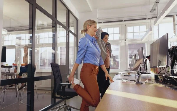 Zwei Frauen stehen im Büro am Schreibtisch und dehnen sich