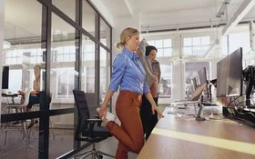 Zwei Frauen stehen im Büro am Schreibtisch und dehnen sich