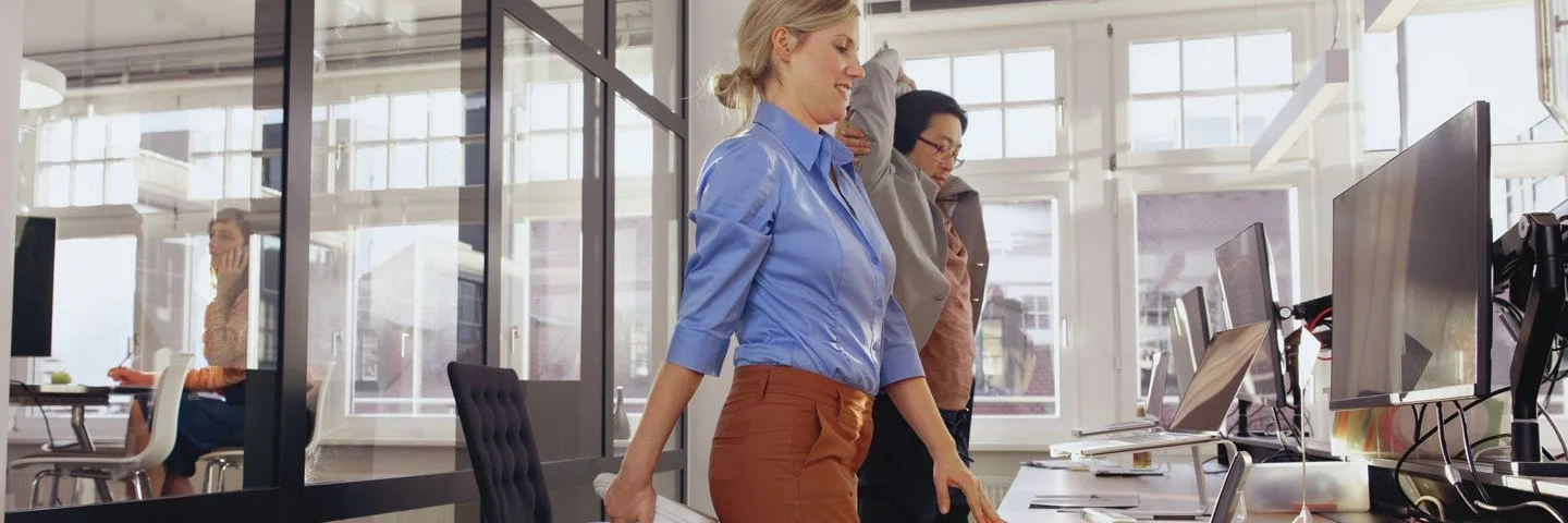 Zwei Frauen stehen im Büro am Schreibtisch und dehnen sich