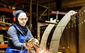 Eine Frau mit Schutzkleidung, Gehörschutz und Schutzbrille beim Schweißen