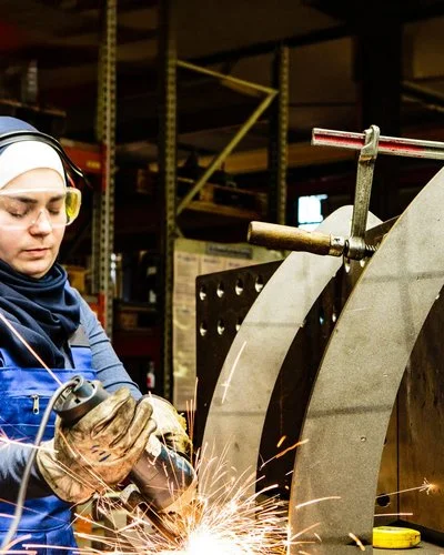 Eine Frau mit Schutzkleidung, Gehörschutz und Schutzbrille beim Schweißen
