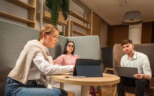 Drei Auszubildende sitzen vor Table-PCs an einem Besprechungstisch