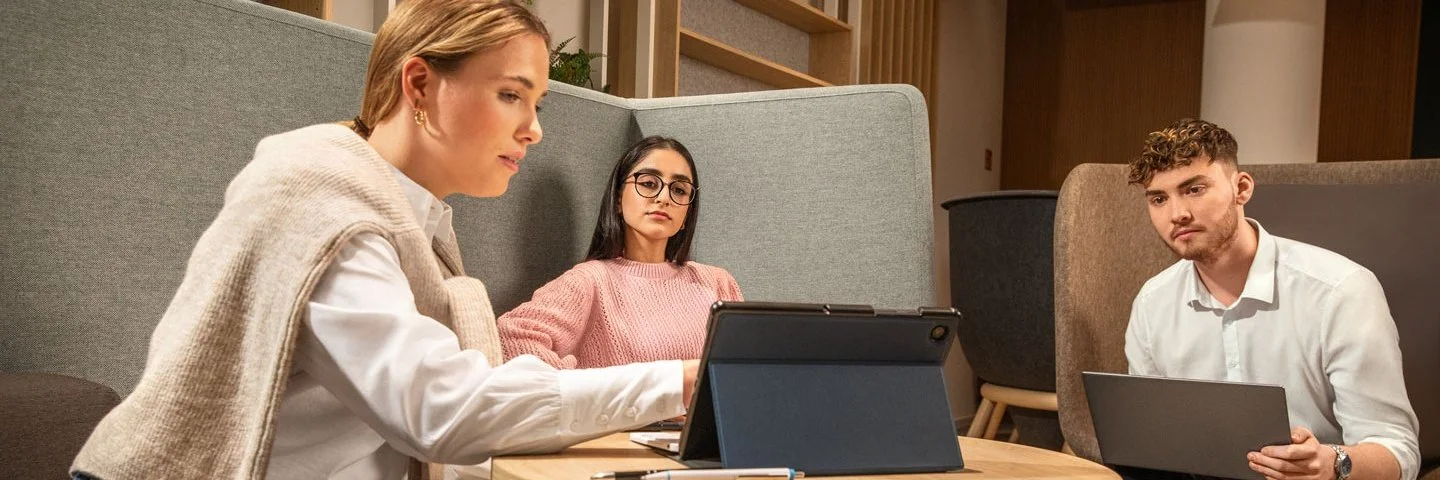 Drei Auszubildende sitzen vor Table-PCs an einem Besprechungstisch