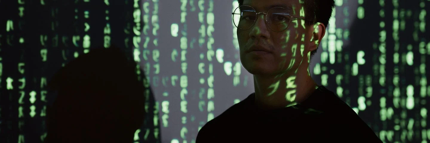 Person sitzt im Halbdunkeln, beleuchtet von digitalen Zeichen
