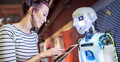 KI und Arbeit: Frau mit Tablet vor einem humanoiden Roboter