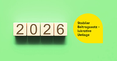 Beitragssatz 2026: Holzbausteine mit der Jahreszahl 2026 neben einem gelben Textfeld mit der Aufschrift „Stabiler Beitragssatz – lukrative Umlage“ auf grünem Hintergrund.