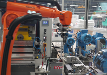 Ein Industrieroboter in einer automatisierten Produktionszelle. Der Roboterarm ist orange und befindet sich in der Nähe einer Maschine mit blauen Motoren.