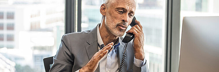 Ein weißhaariger Mann telefoniert in einem Büro.