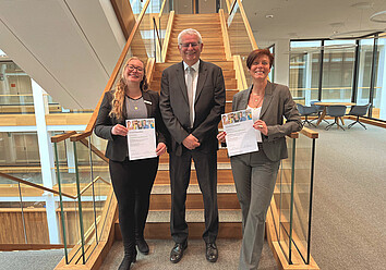 Lilli Mazurek, Frank Fastenau und Kerstin Akkermann (von links) freuen sich über die Qualifikation zu „Betrieblichen Gesundheitscoaches“. Links und rechts von einem lächelnden Mann stehen zwei lächelnde Frauen, die Zertifikate in die Kamera halten.