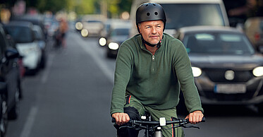 Mann fährt mit dem Fahrrad auf einer belebten Straße.