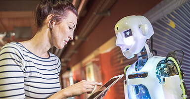 KI und Arbeit: Frau mit Tablet vor einem humanoiden Roboter