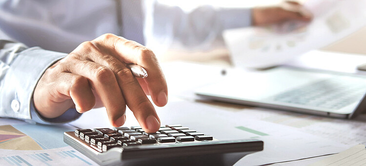 Online-Seminar „Praxistipps für die Entgeltabrechnung“: Mann am Schreibtisch tippt auf einem Taschenrechner