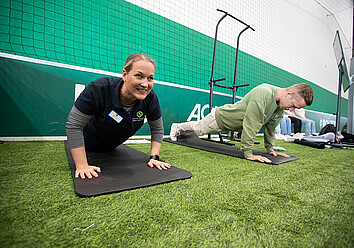 Gesundheitstag: Zwei Menschen planken in einer Sporthalle. Gesundheitstag: Zwei Menschen planken in einer Sporthalle.
