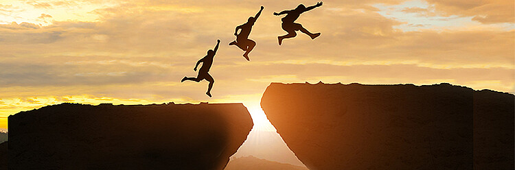 Drei Menschen springen über einen Felsspalt im Sonnenuntergang