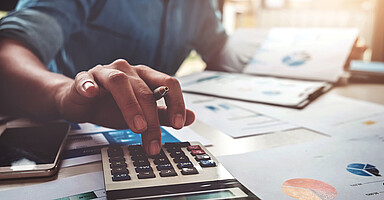 Klage gegen Finanzlücke: Ein Mann an einem Schreibtisch mit vielen Unterlagen tippt auf einen Taschenrechner.