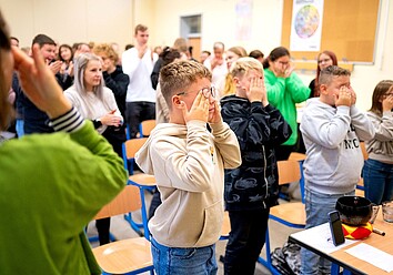 Projekt ABiK der Uni Leipzig: Kinder und Erwachsene befinden sich in einem Klassenzimmer und machen gemeinsam eine Übung, bei der sich die Kinder die Augen zuhalten Projekt ABiK der Uni Leipzig: Kinder und Erwachsene befinden sich in einem Klassenzimmer und machen gemeinsam eine Übung, bei der sich die Kinder die Augen zuhalten