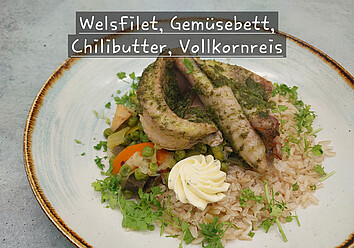 Auf einem Teller ist ein Gericht aus Welsfilet auf einem Gemüsebett mit Chilibutter und Vollkornreis angerichtet