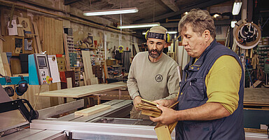 Online-Seminar „Personaleinsatz bei anderen Arbeitgebern“: Zwei Männer besprechen sich in einer Werkstatt.