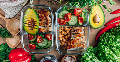 Auf dem Bild sind sind zwei Schalen mit vorbereitetem, gesunden Essen zu sehen und jede Menge unterschiedliches Gemüse und Salat.