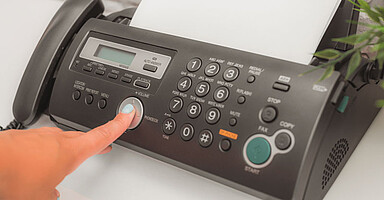 Schluss mit Faxen: Eine Hand drückt eine Taste eines Faxgerätes