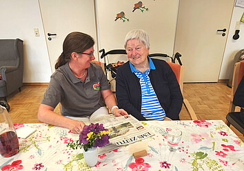 Alltagssituation in der Pflege Pflegefachkraft liest Bewohnerin eine Zeitung vor