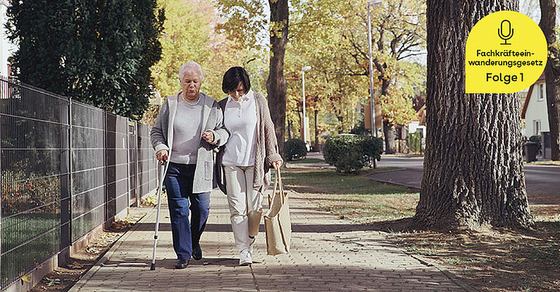 Eine Pflegekraft unterstützt eine Seniorin beim Spaziergang.