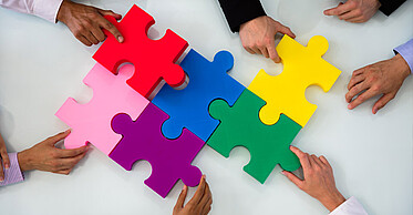 Eine diverse Gruppe Menschen zeigt anhand von einem Puzzle die Zusammenarbeit im Unternehmen