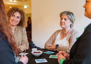 Mehrere Personen stehen um einen Bistrotisch und unterhalten sich