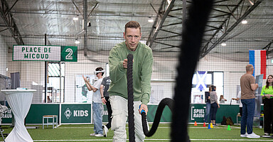 Gesundheitstag im Unternehmen: junger Mann trainiert an einem Seil in einer Sporthalle Gesundheitstag im Unternehmen: junger Mann trainiert an einem Seil in einer Sporthalle
