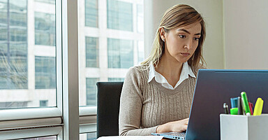 Betriebsprüfung: Junge Frau sitzt im Büro und blickt prüfend auf einen Laptop 