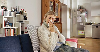 Fehlzeiten-Report der AOK: Frau sitzt schnäuzend auf heimischem Sofa.
