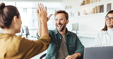 Mit Teamship zu gesunder Unternehmenskultur Ein Mann und ein Frau geben sich lachend ein „High Five“