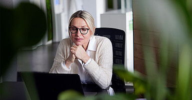 Wechseljahre – Frau schaut nachdenklich am Schreibtisch sitzend auf den Monitor