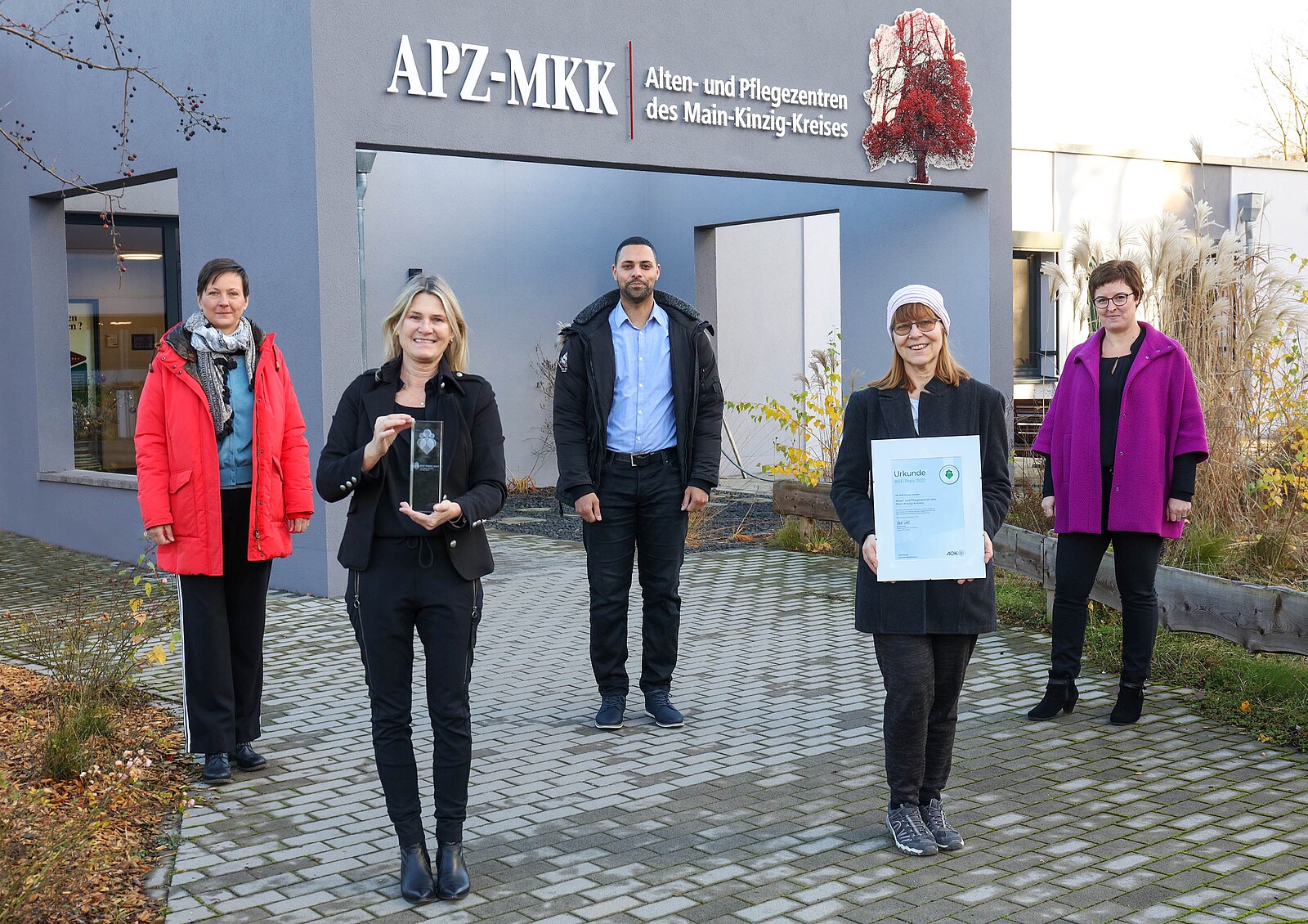 Alten- & Pflegezentren Main-Kinzig-Kreis: Fünf Menschen mit Urkunde und Preis vor Gebäude