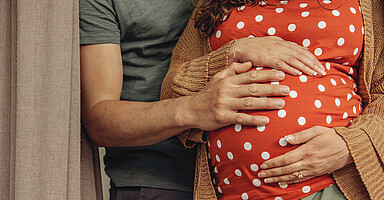 Mutter und Vater halten ihre Hände auf den schwangeren Bauch.