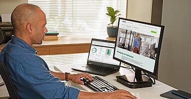 Homeoffice: Mann sitzt am heimischen Schreibtisch mit zwei Bildschirmen