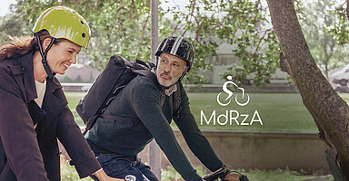 Mit dem Rad zur Arbeit: Eine junge Frau und ein älterer Mann radeln durch einen Park