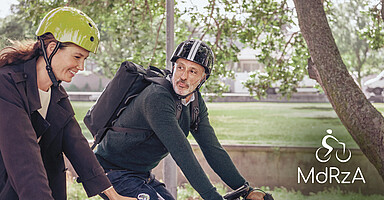 Mit dem Rad zur Arbeit: Eine junge Frau und ein älterer Mann radeln durch einen Park