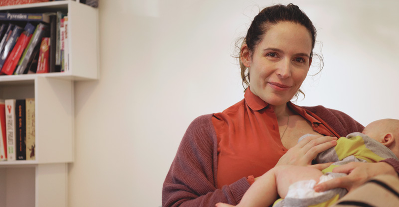Lächelnde Mutter stillt ihr Baby in einem Ruheraum am Arbeitsplatz.