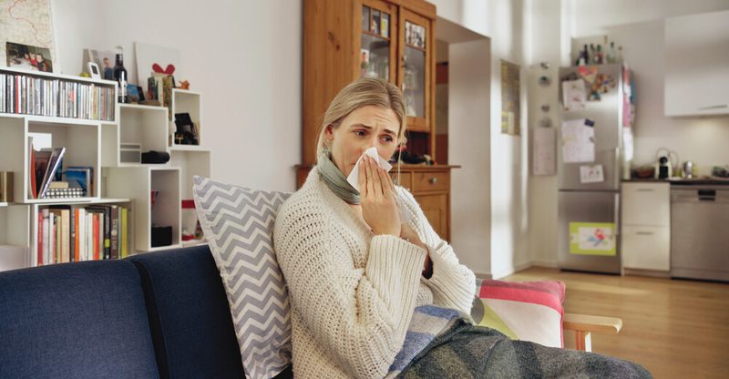 Fehlzeiten-Report der AOK: Frau sitzt schnäuzend auf heimischem Sofa. Fehlzeiten-Report der AOK: Frau sitzt schnäuzend auf heimischem Sofa.