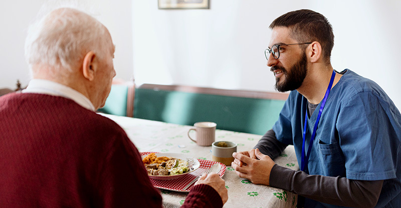 Ausländische Fachkräfte: Ein Pfleger sitzt bei einem Senior, der gerade isst
