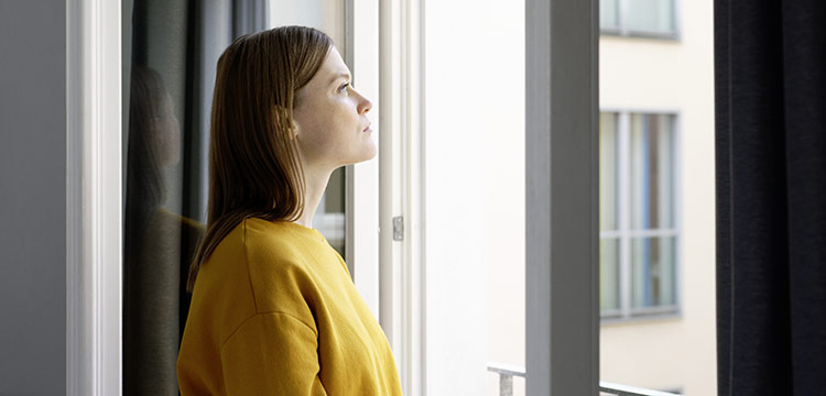 Bei Quarantäne müssen Mitarbeiter zuhause bleiben. Eine junge Frau starrt aus dem Fenster ihrer Wohnung