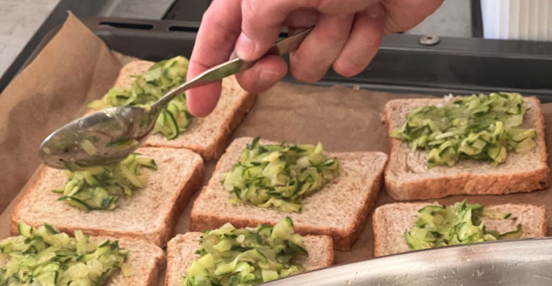 Ein Gurkensalat wird auf mehrere Scheiben Brot verteilt.