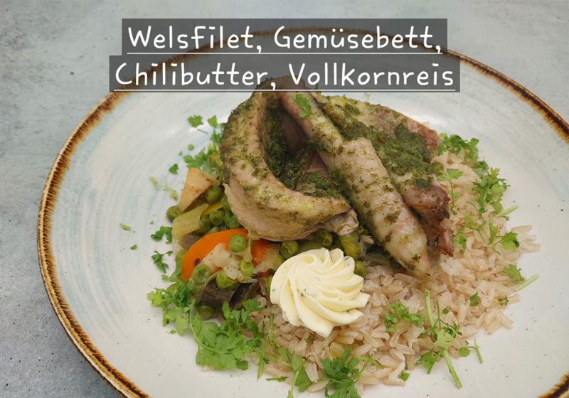 Auf einem Teller ist ein Gericht aus Welsfilet auf einem Gemüsebett mit Chilibutter und Vollkornreis angerichtet