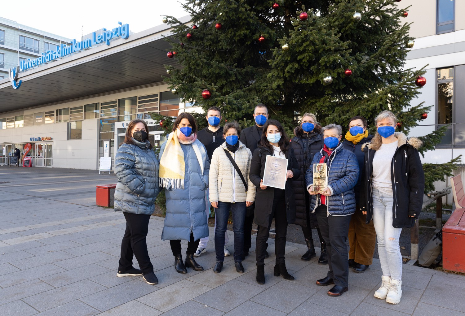 Uniklinikum Leipzig: Zehn Personen mit Masken vor Weihnachtsbaum