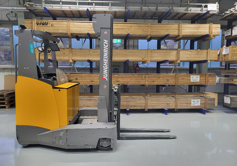 Ein Gabelstapler der Marke Jungheinrich steht in einem Lager vor Regalen mit Holzpaletten.