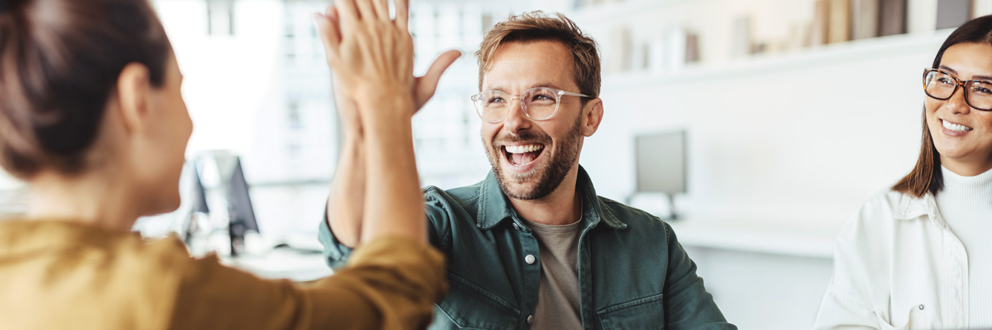 Mit Teamship zu gesunder Unternehmenskultur Ein Mann und ein Frau geben sich lachend ein „High Five“