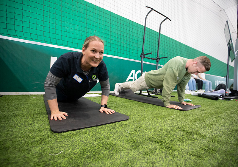 Gesundheitstag: Zwei Menschen planken in einer Sporthalle. Gesundheitstag: Zwei Menschen planken in einer Sporthalle.