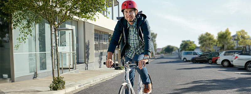Mann mit rotem Fahrradhelm sitzt auf dem Fahrrad und fährt gerade zur Arbeit