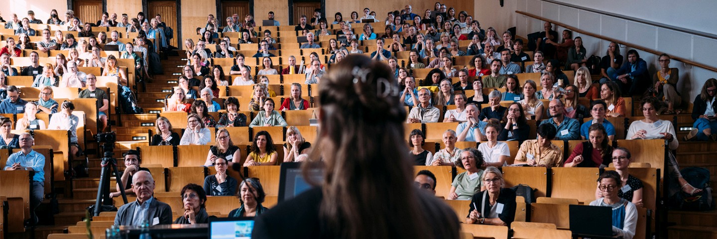 Projekt ABiK der Uni Leipzig: Eine Frau spricht vor einem großem Publikum in einem Hörsaal Projekt ABiK der Uni Leipzig: Eine Frau spricht vor einem großem Publikum in einem Hörsaal